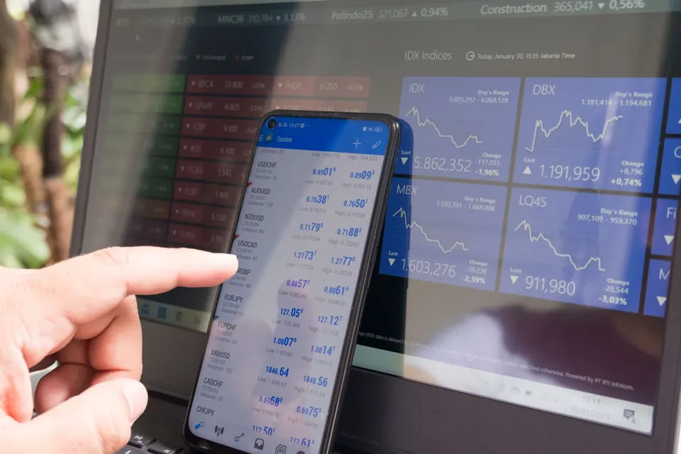 A trader reviewing market information on a phone beside a laptop
